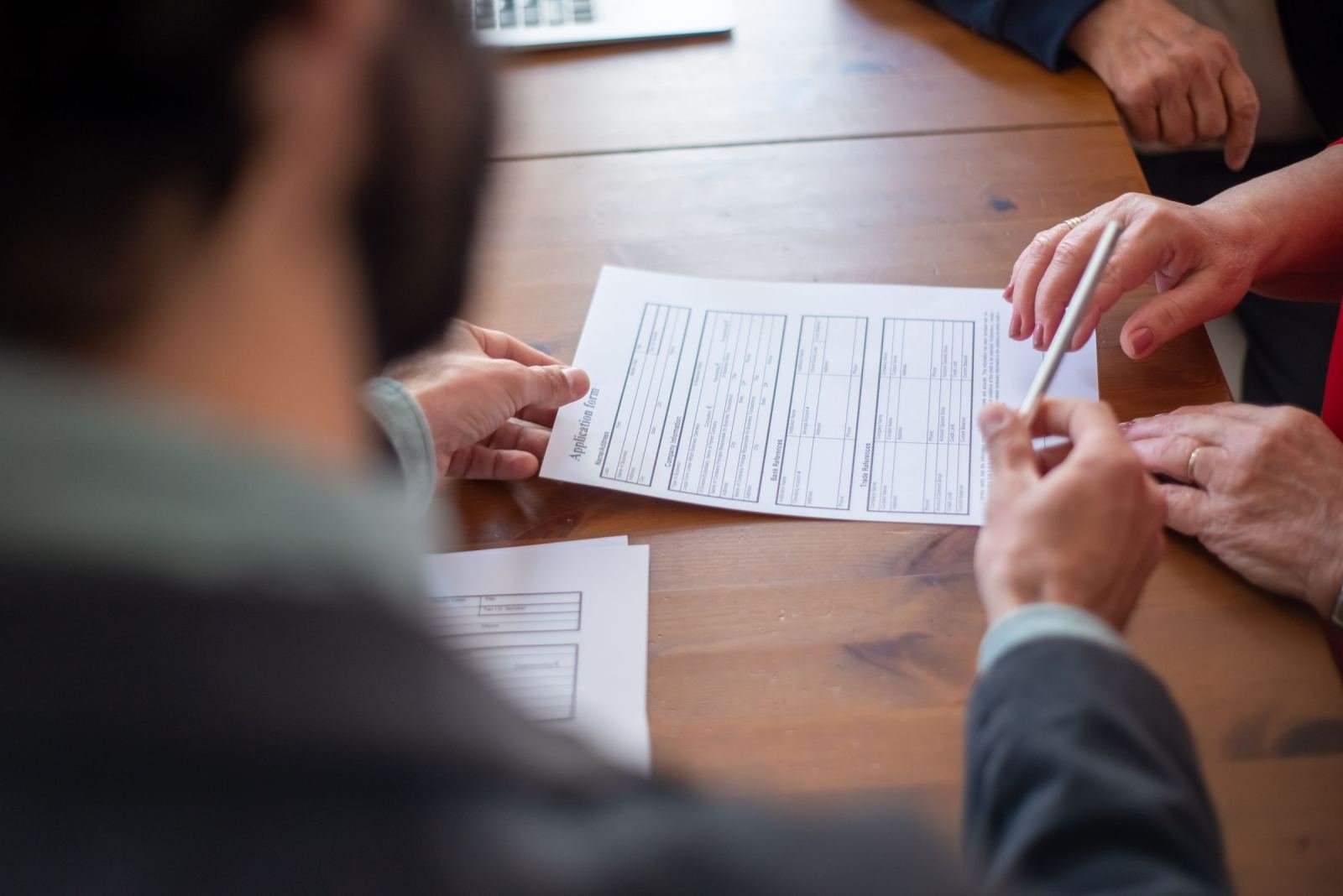 Two people review a printed application form on a wooden table