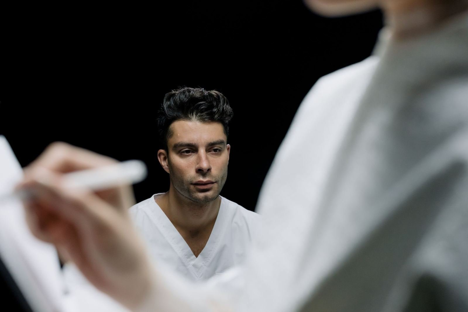 A clinician in a white coat looks on as another person writes notes