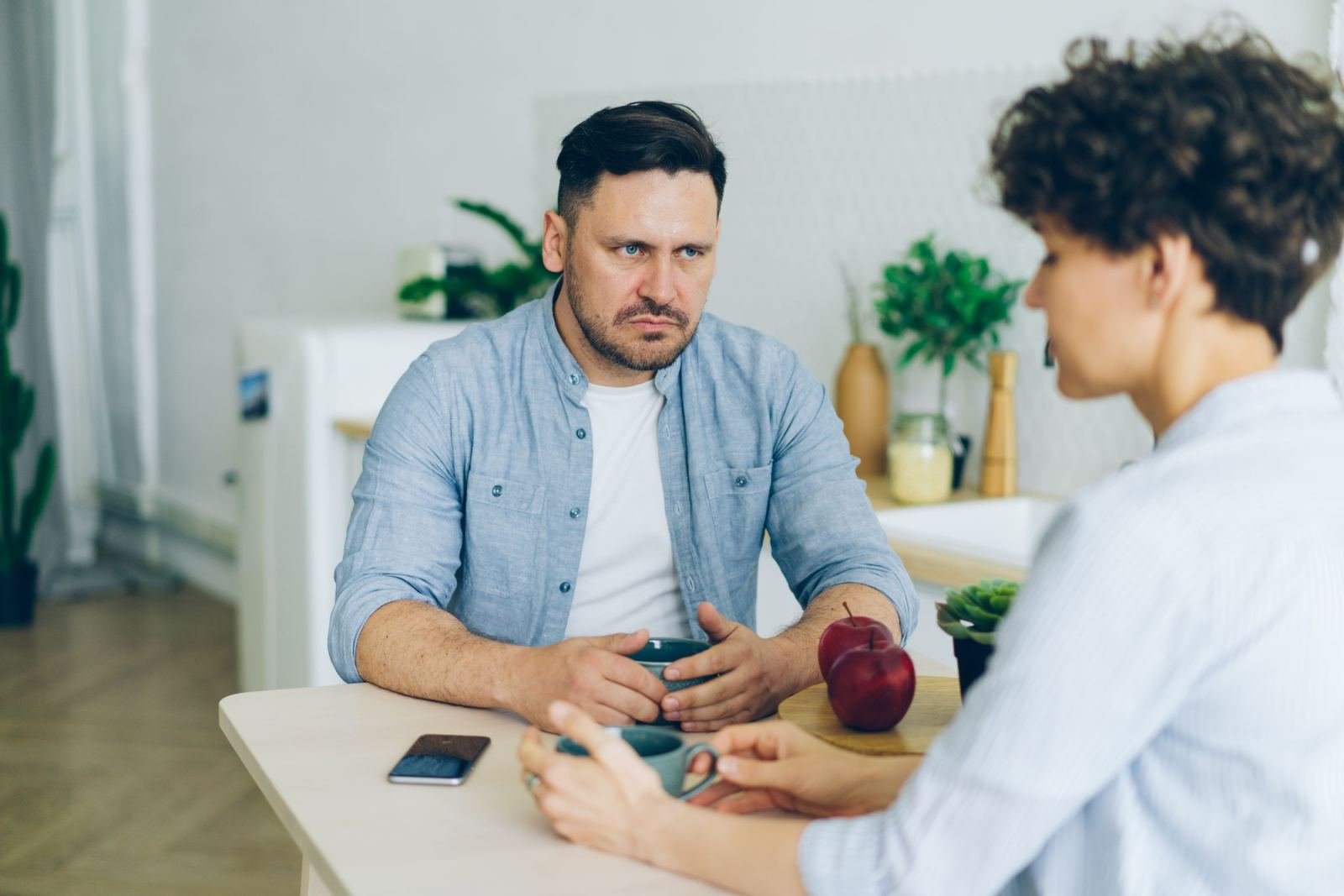 A man and woman are seated at a table with mugs, engaged in a serious talk.