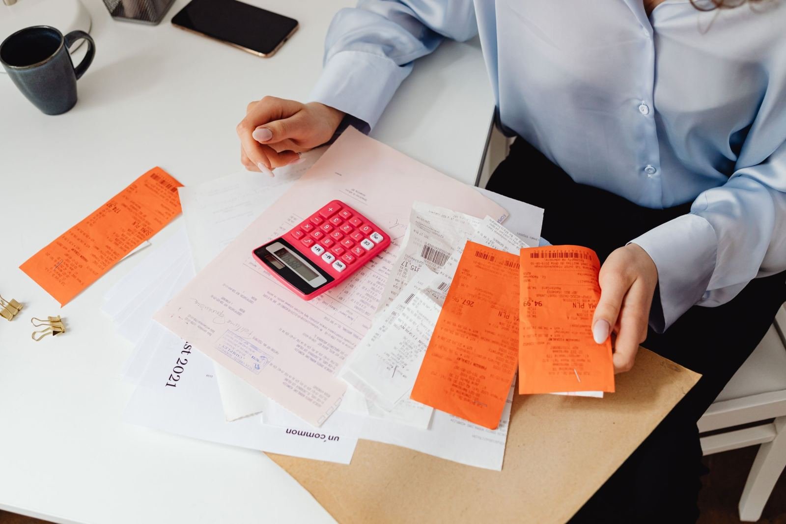 A person at a desk with a pink calculator and orange receipts
