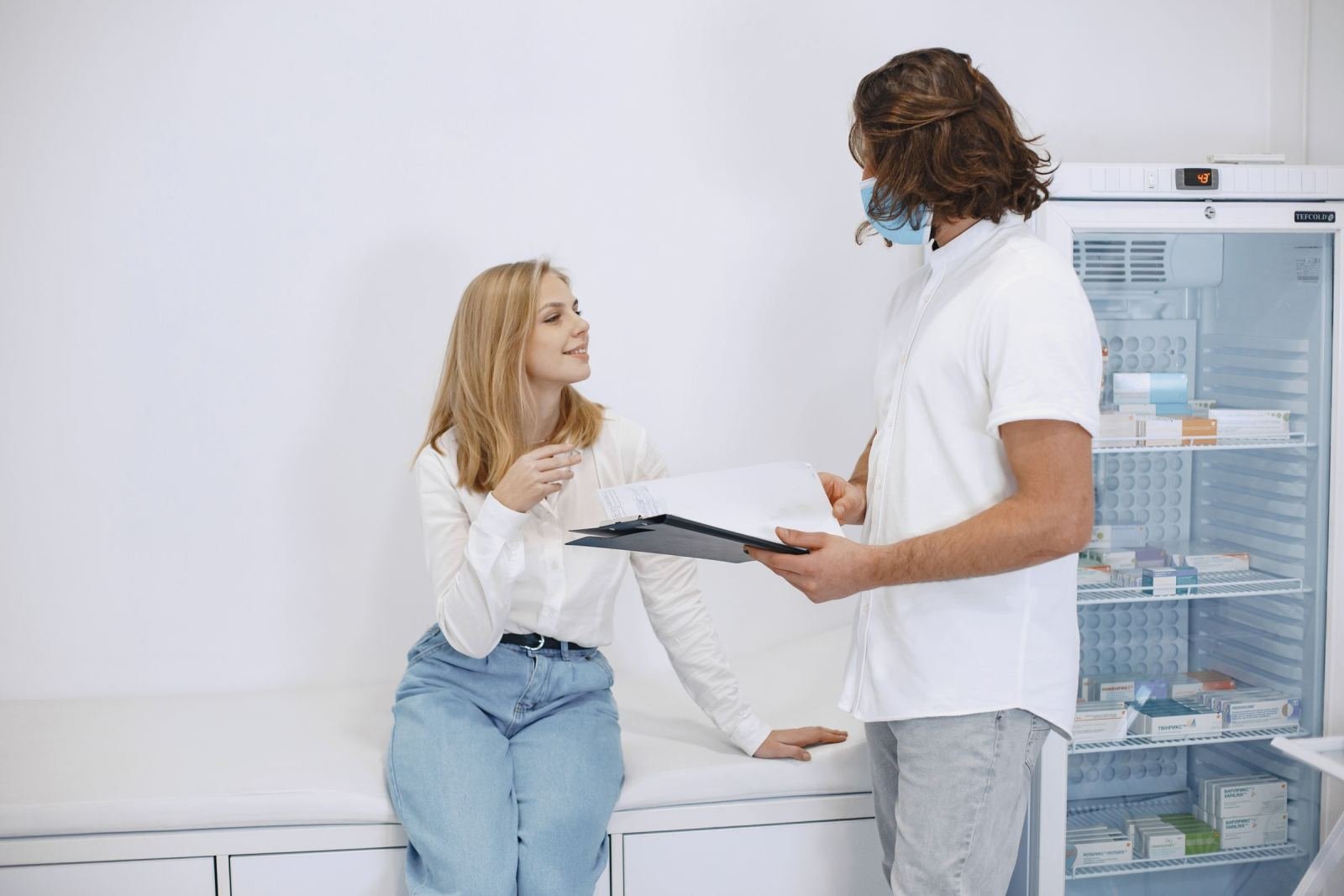 A woman talks with a pharmacist wearing a mask in a medical consultation room