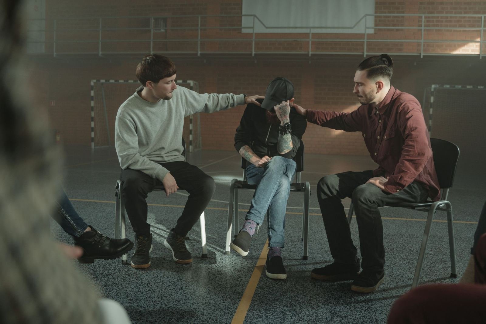 Three men sit in a circle with two men offering support to a man leaning forward