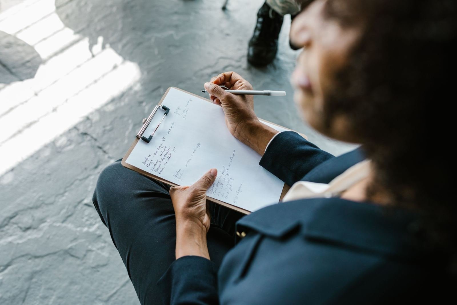 A person in a blazer writes notes on a clipboard