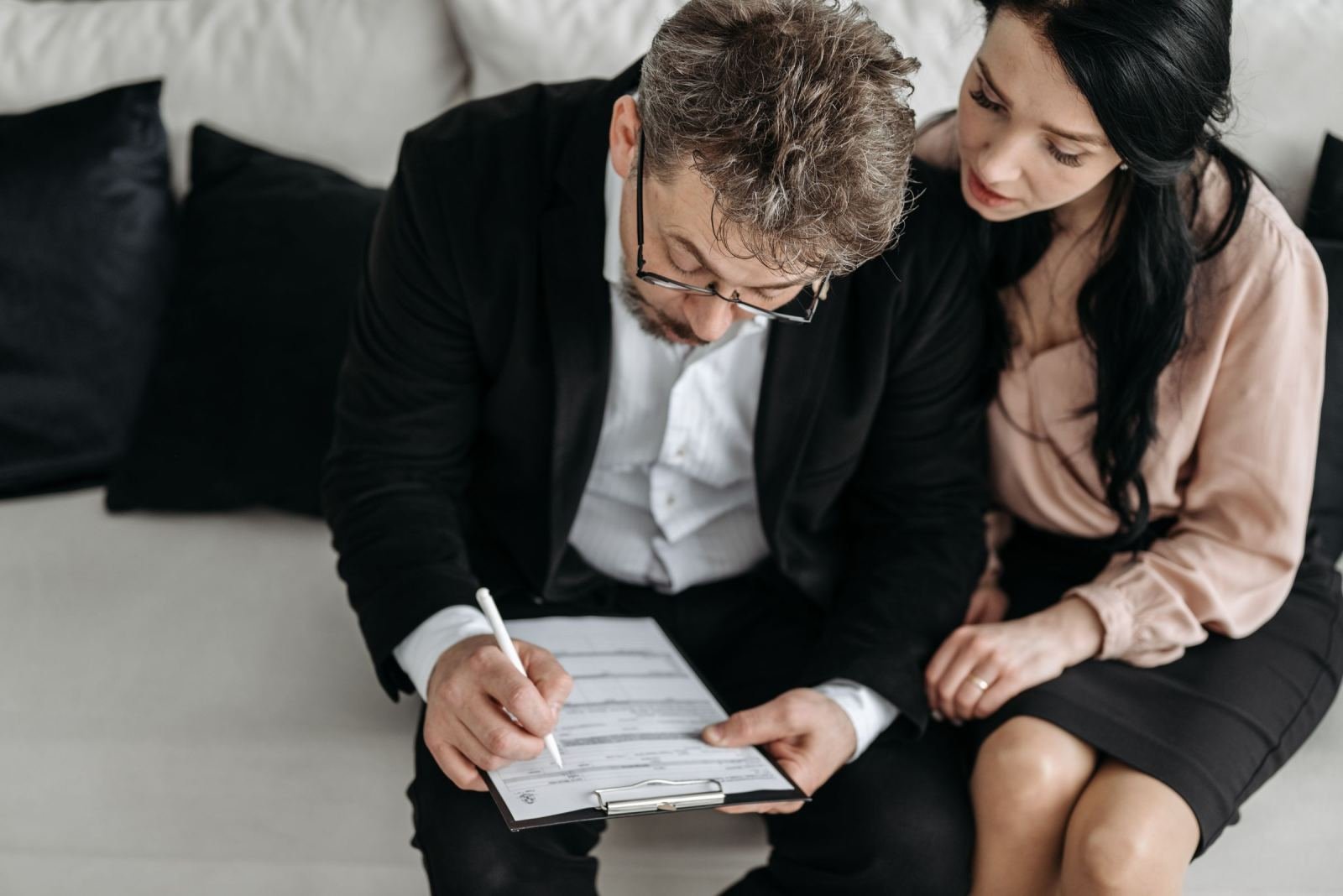 A man and woman review a document on a clipboard while sitting on a couch