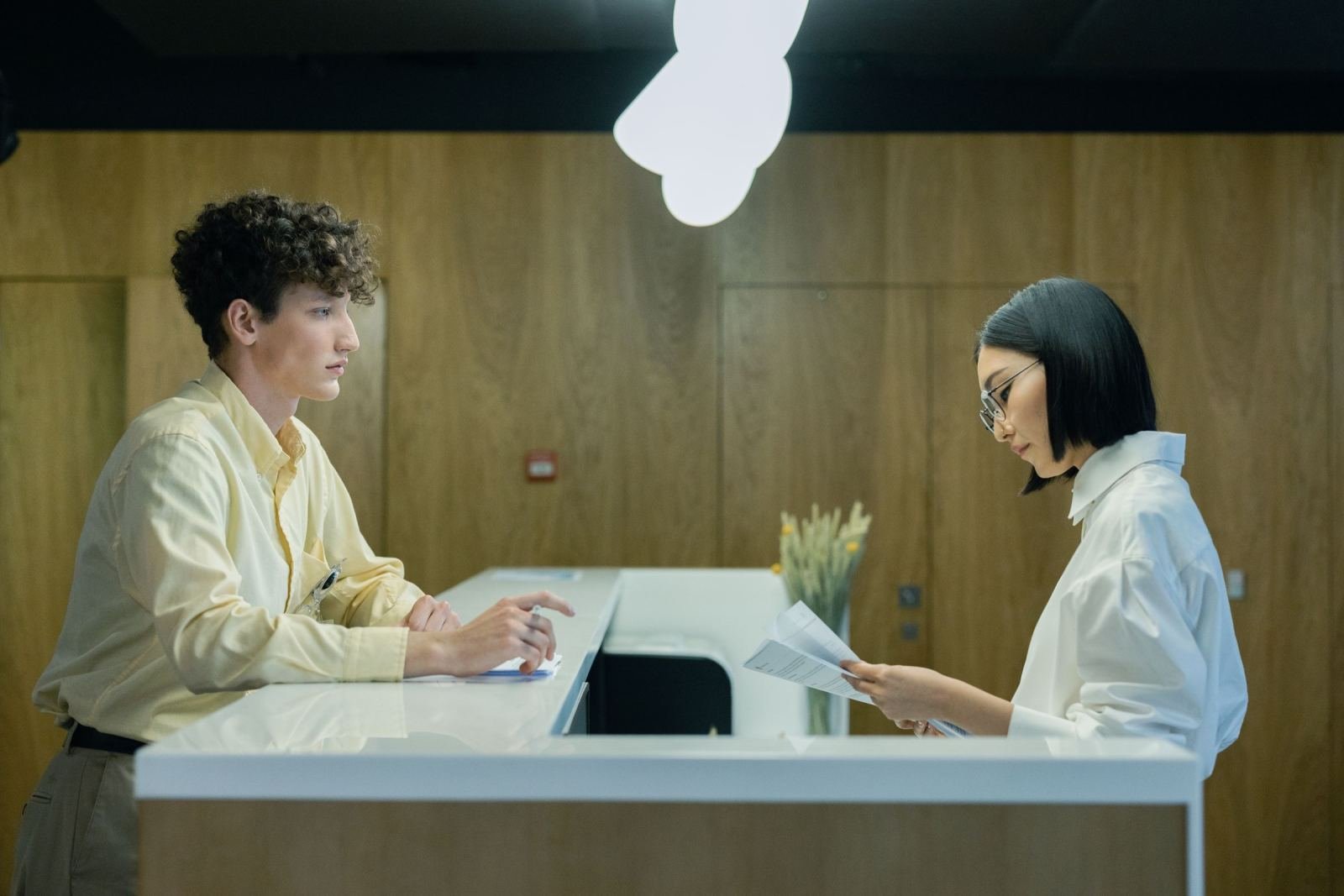 A man speaks with a staff member at a white reception counter