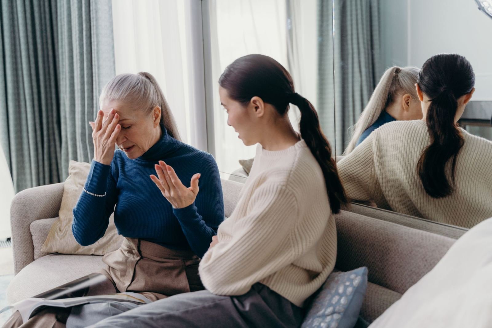 An older woman gestures while talking to a younger woman on a couch