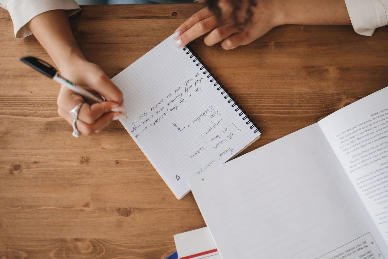 A person writes notes in a spiral notebook on a wooden table