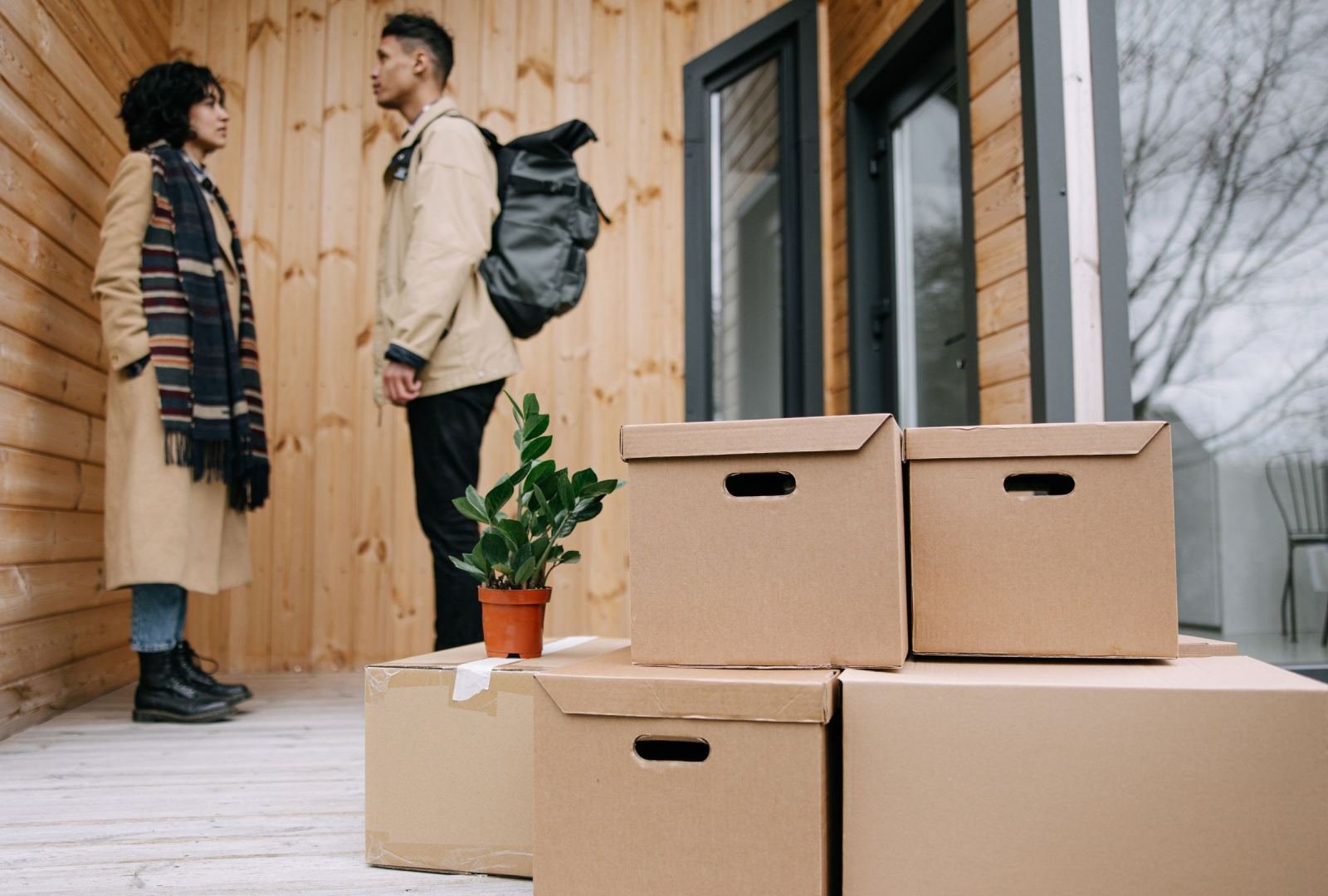 A man and woman stand on a porch next to several cardboard moving boxes