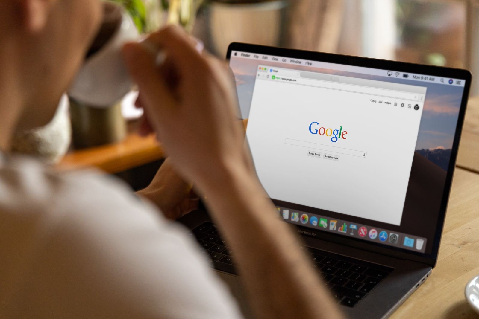 A person holds a mug while using a laptop to search on Google