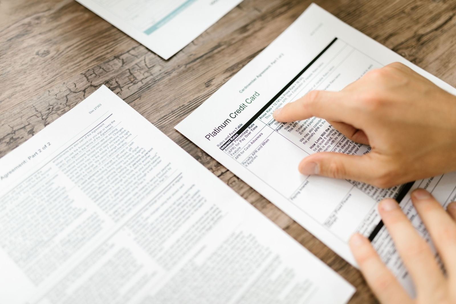 A person points to a credit card agreement document on a wooden desk