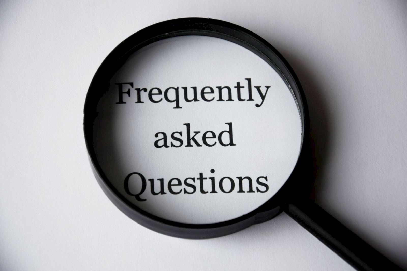 A magnifying glass focusing on the words Frequently asked Questions on white paper