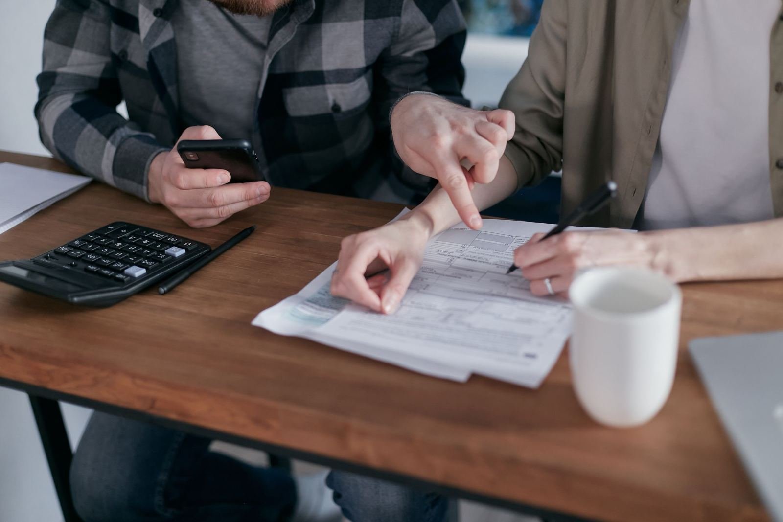 Two people review printed documents and use a calculator at a wooden table