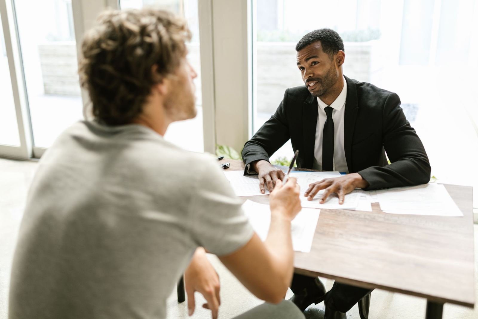 A man in a suit reviews paperwork with a client at a wooden table