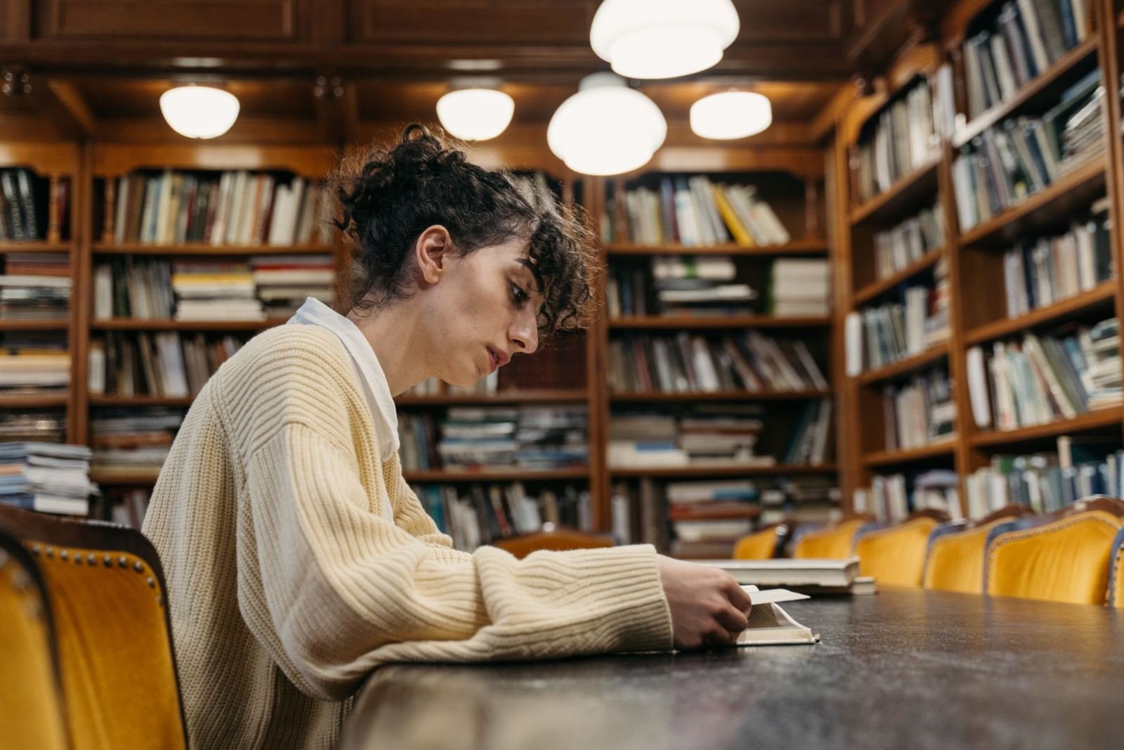 A woman reads a small book while sitting at a table in a library