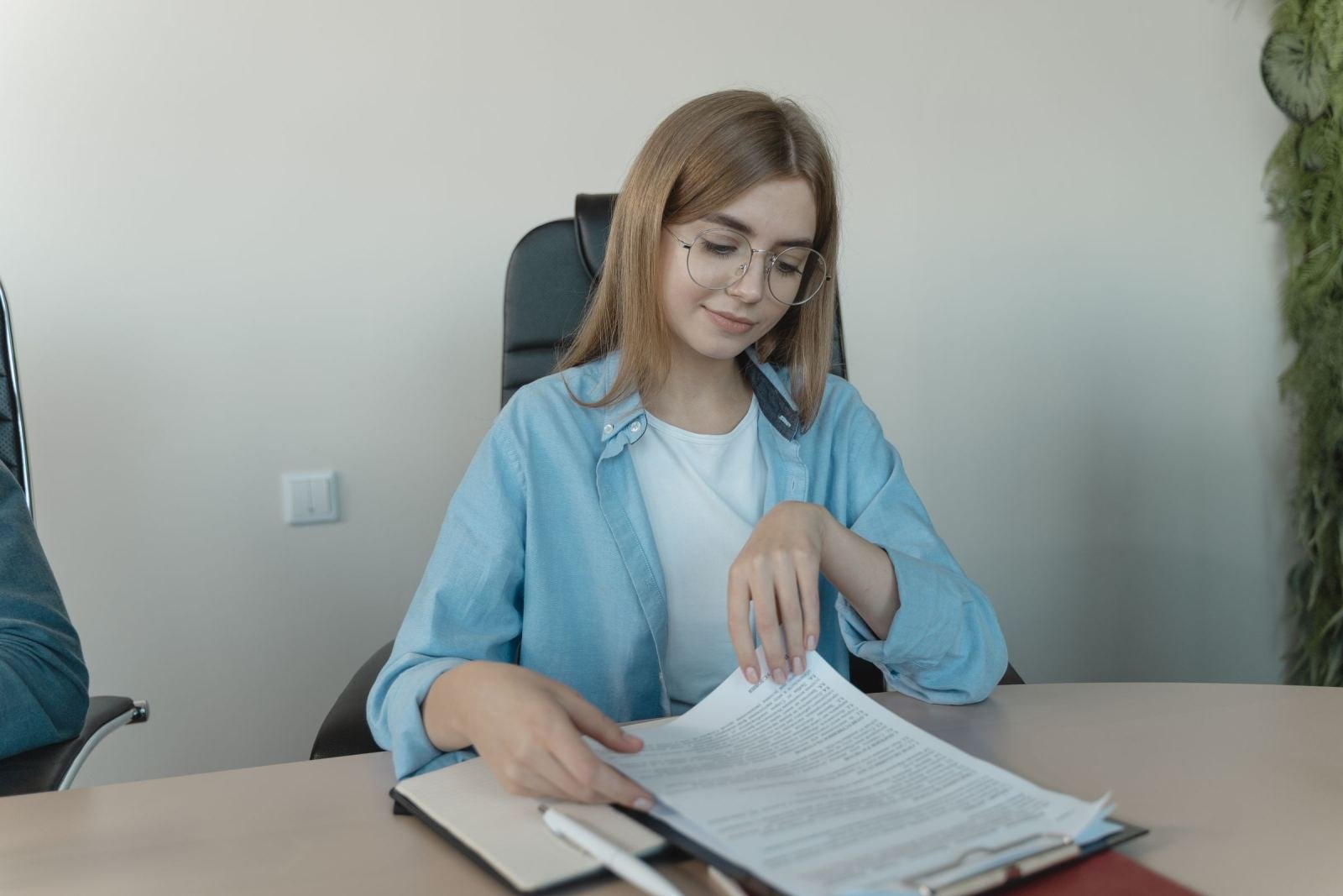A woman with glasses reviews a printed document at a table