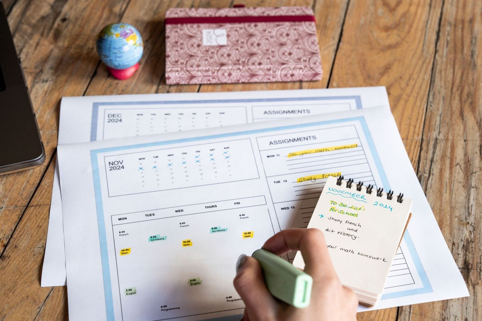 A hand holds a green marker and circles a day on a paper calendar