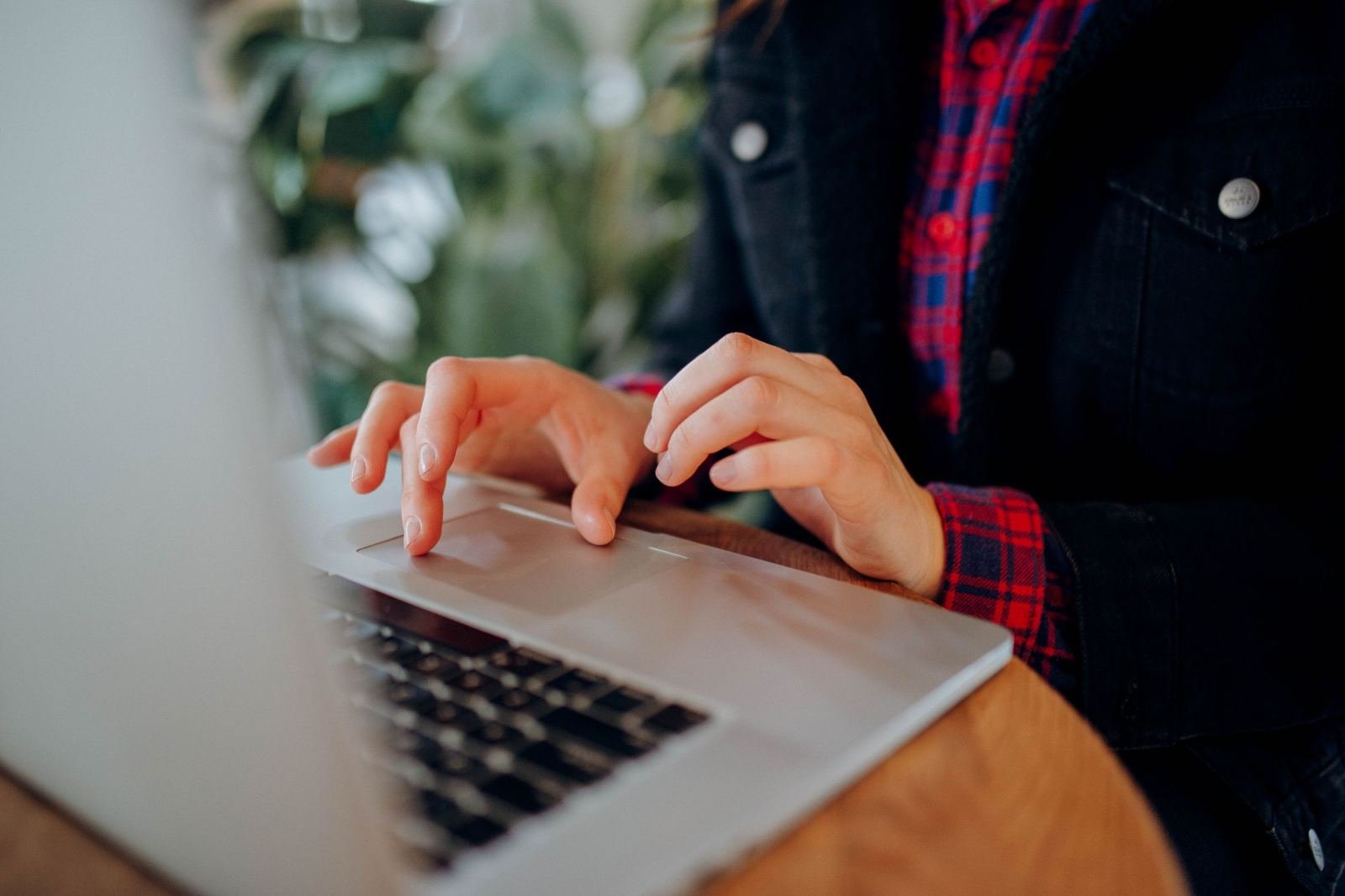 A person in a plaid shirt uses a laptop on a wooden table