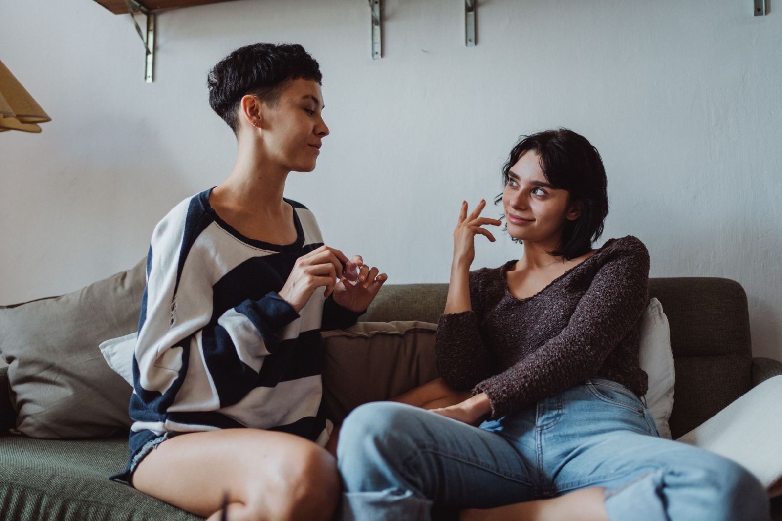Two women chat on a green couch in a well-lit room