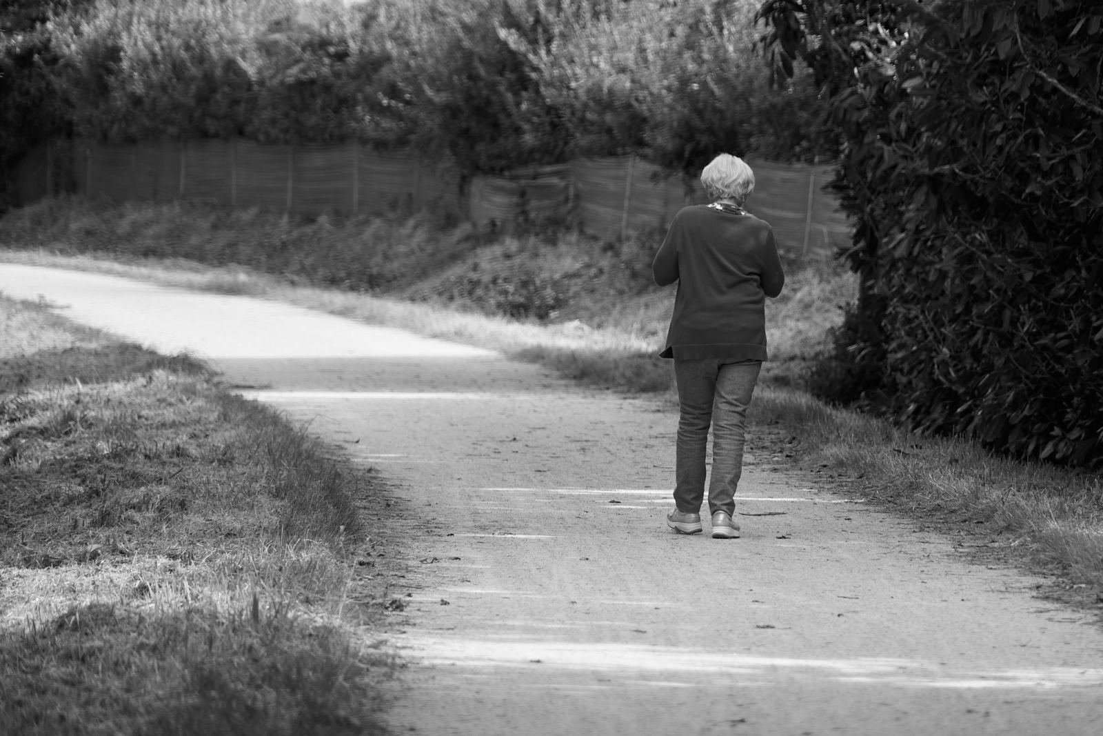 An older person walks away from the camera along a paved outdoor path