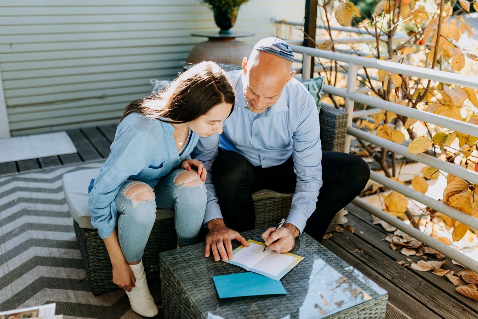 A man and woman look over a notebook together on an outdoor deck
