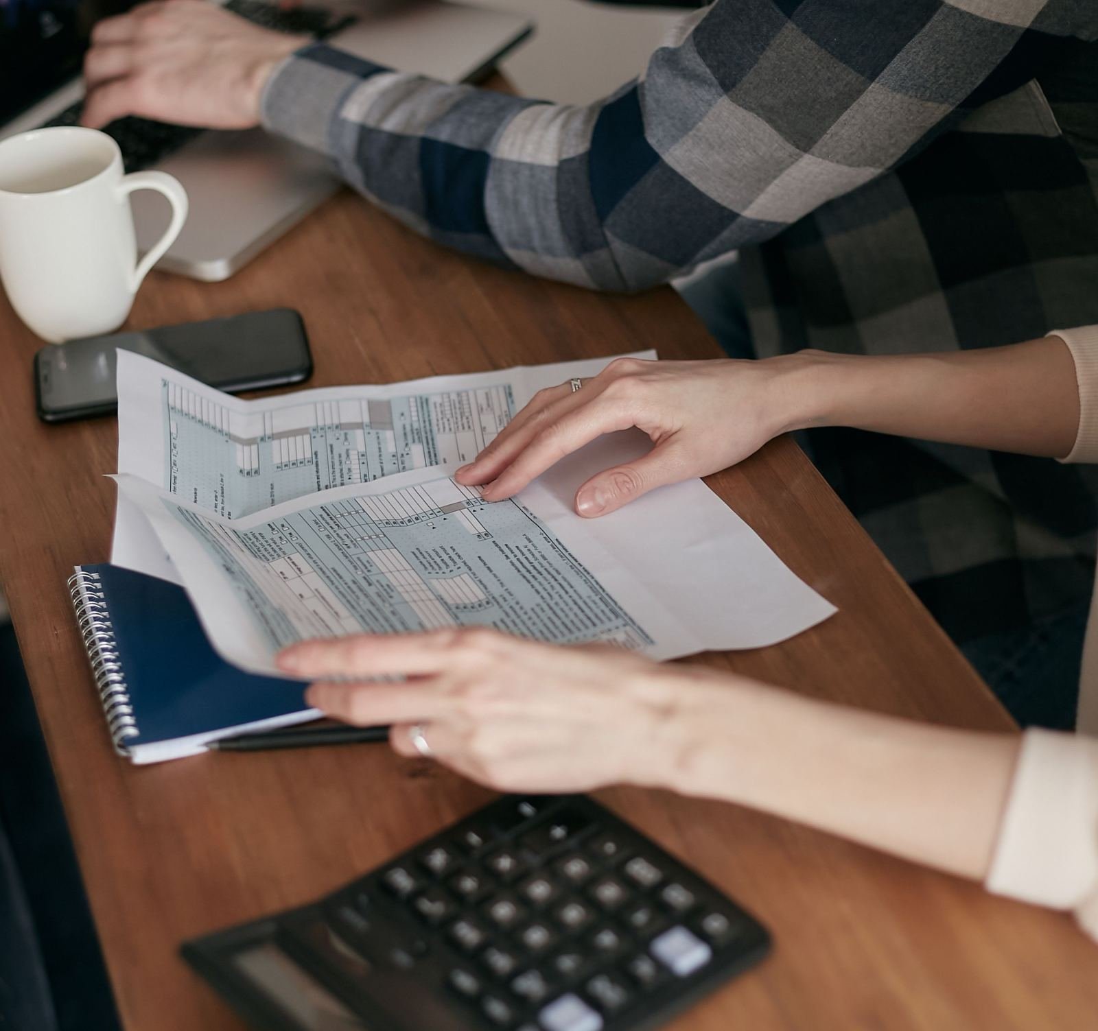 Two people review financial documents and use a calculator at a wooden table
