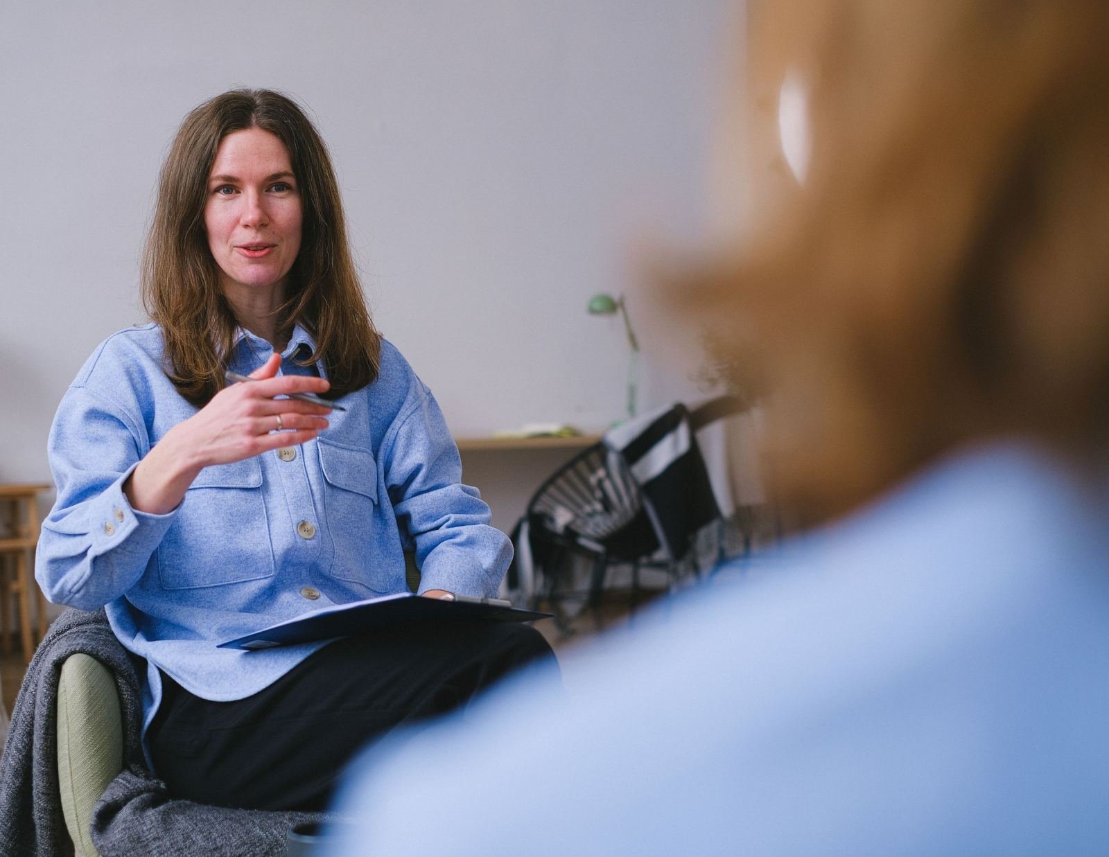 A woman in a blue shirt gestures while speaking to someone in a bright office