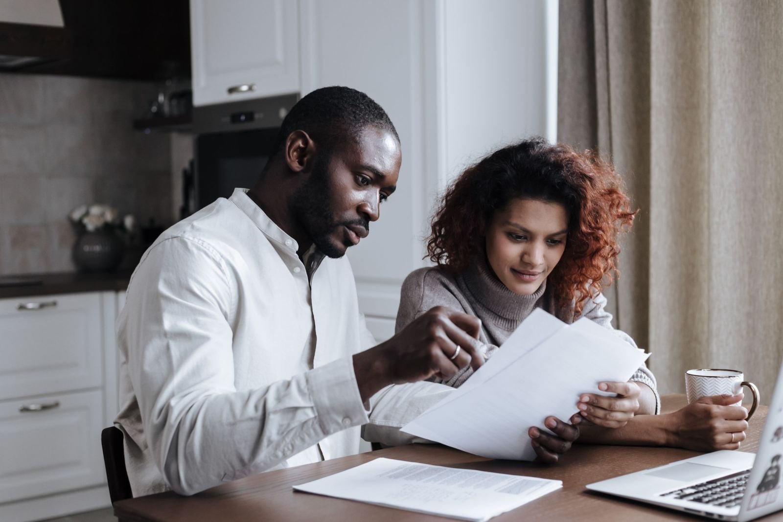 A man and woman review paperwork together at a table with a laptop