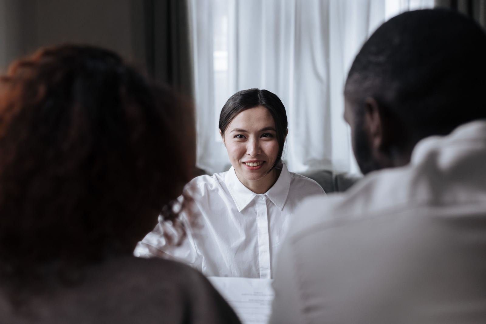 A woman in a white shirt smiles while talking with two other people