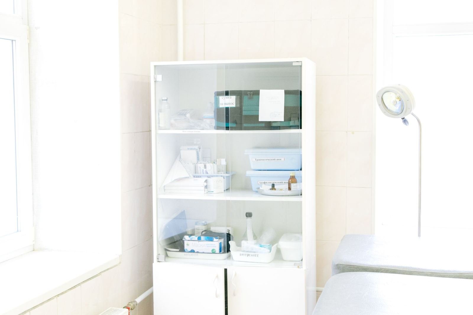 A white medical cabinet filled with supplies next to an exam table