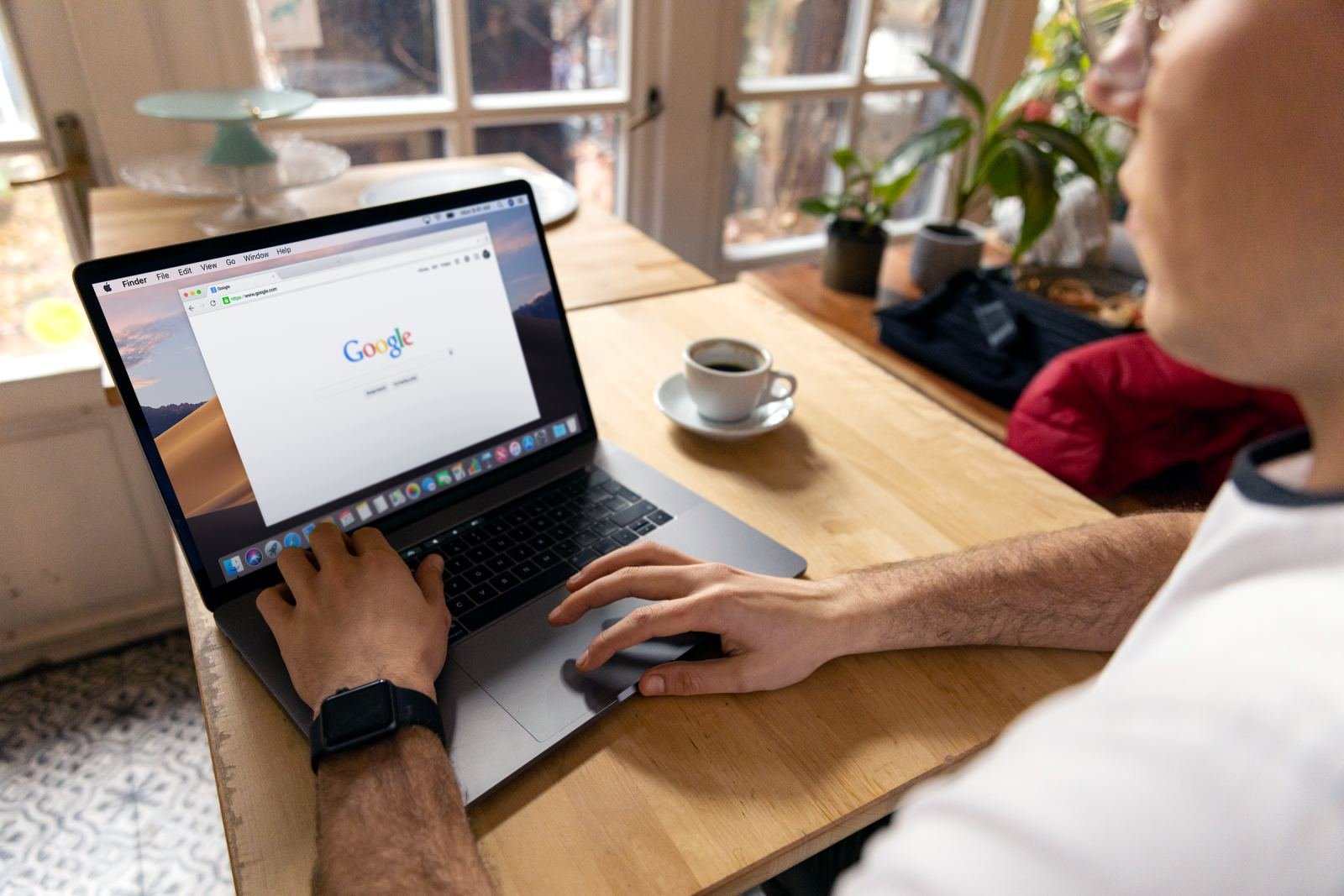 A person uses a laptop at a wooden table with a cup of coffee nearby