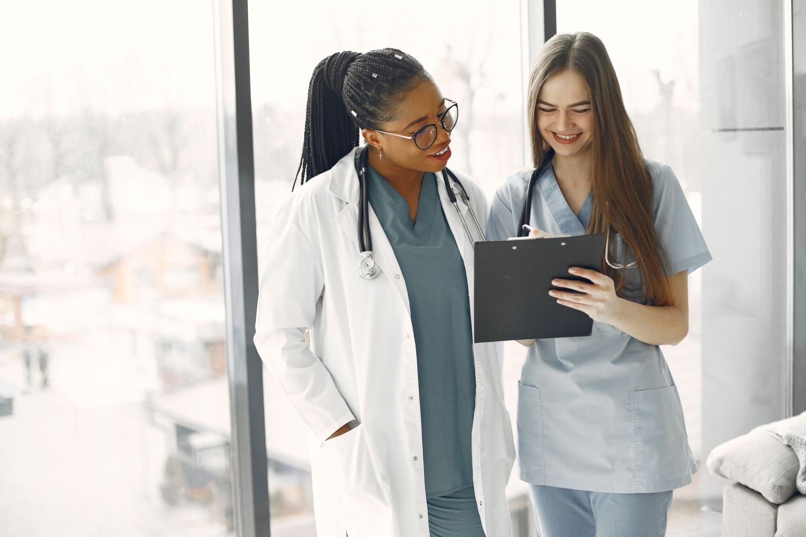 Two medical professionals in scrubs review a clipboard in a bright office