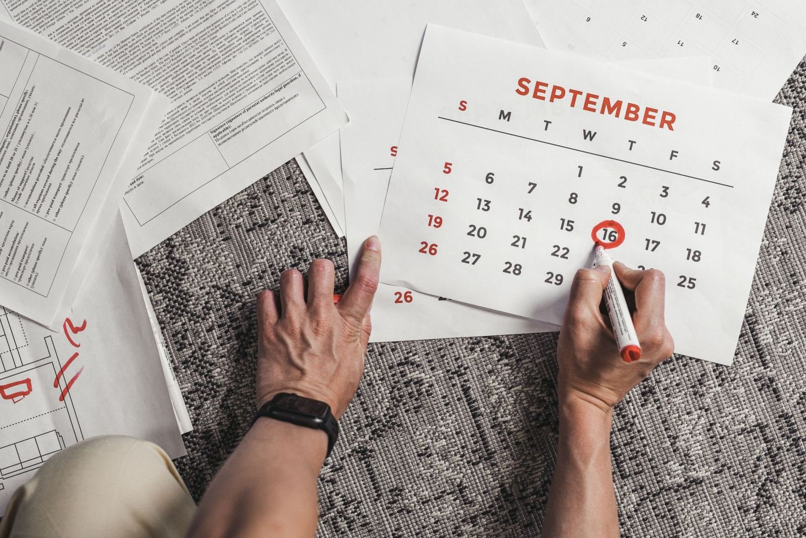 Hands circling a date on a September calendar surrounded by paperwork
