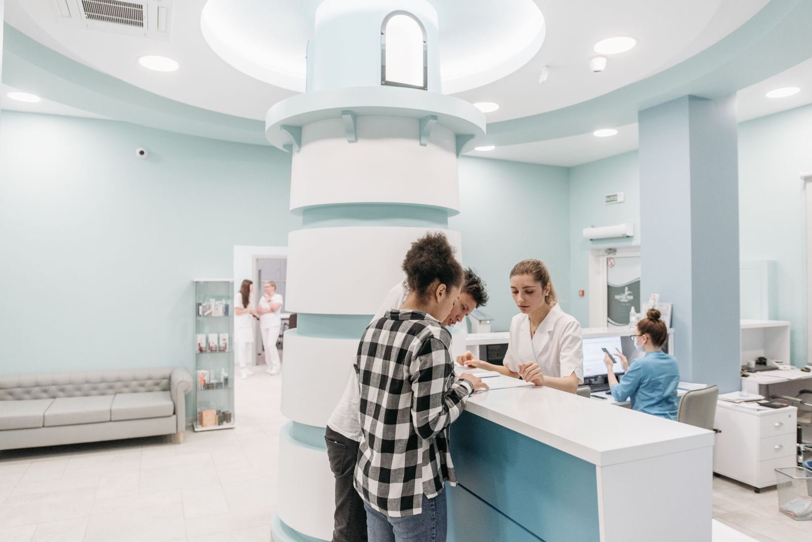 A woman in a plaid shirt checks in at a medical reception desk with a staff member