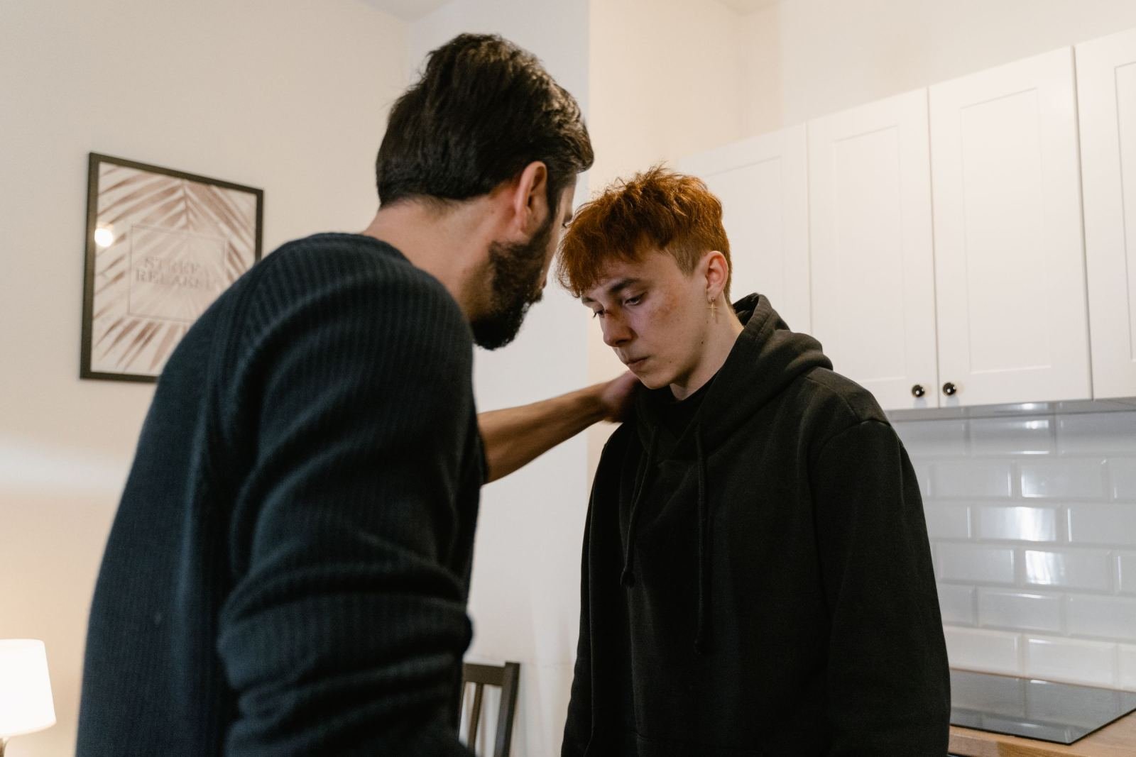 A man places a supportive hand on the shoulder of a younger person in a black hoodie