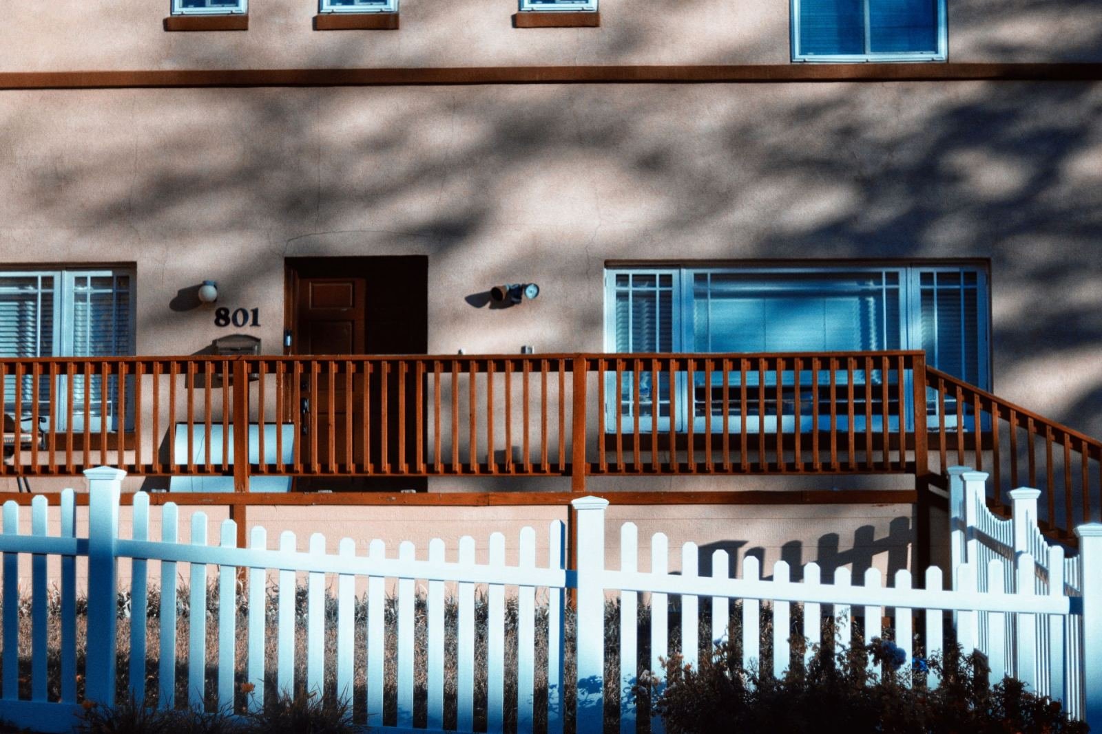 A beige house with a wooden deck and a white picket fence