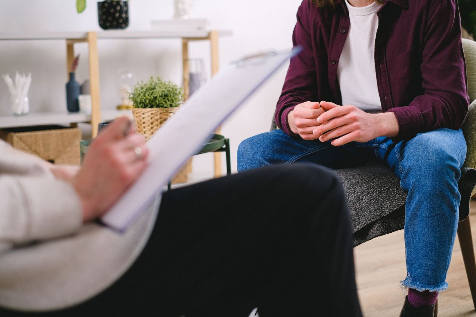 A person with a clipboard talks with someone sitting in a grey chair