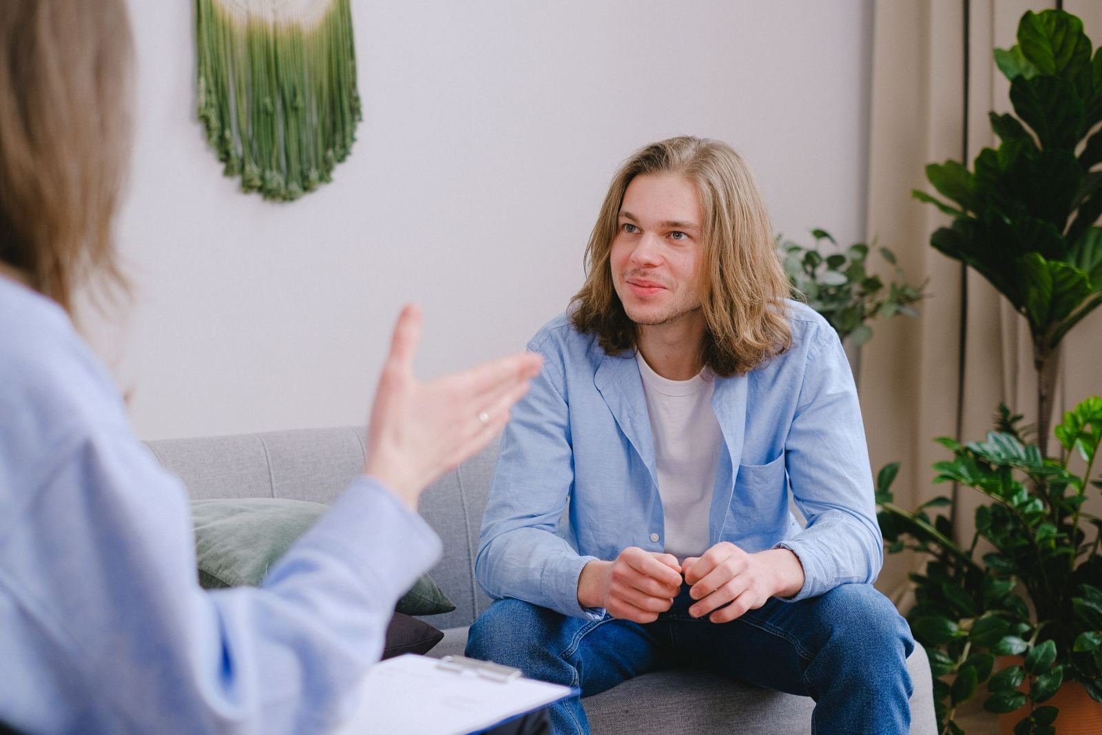 A man sits on a sofa and listens to a woman gesturing during a conversation