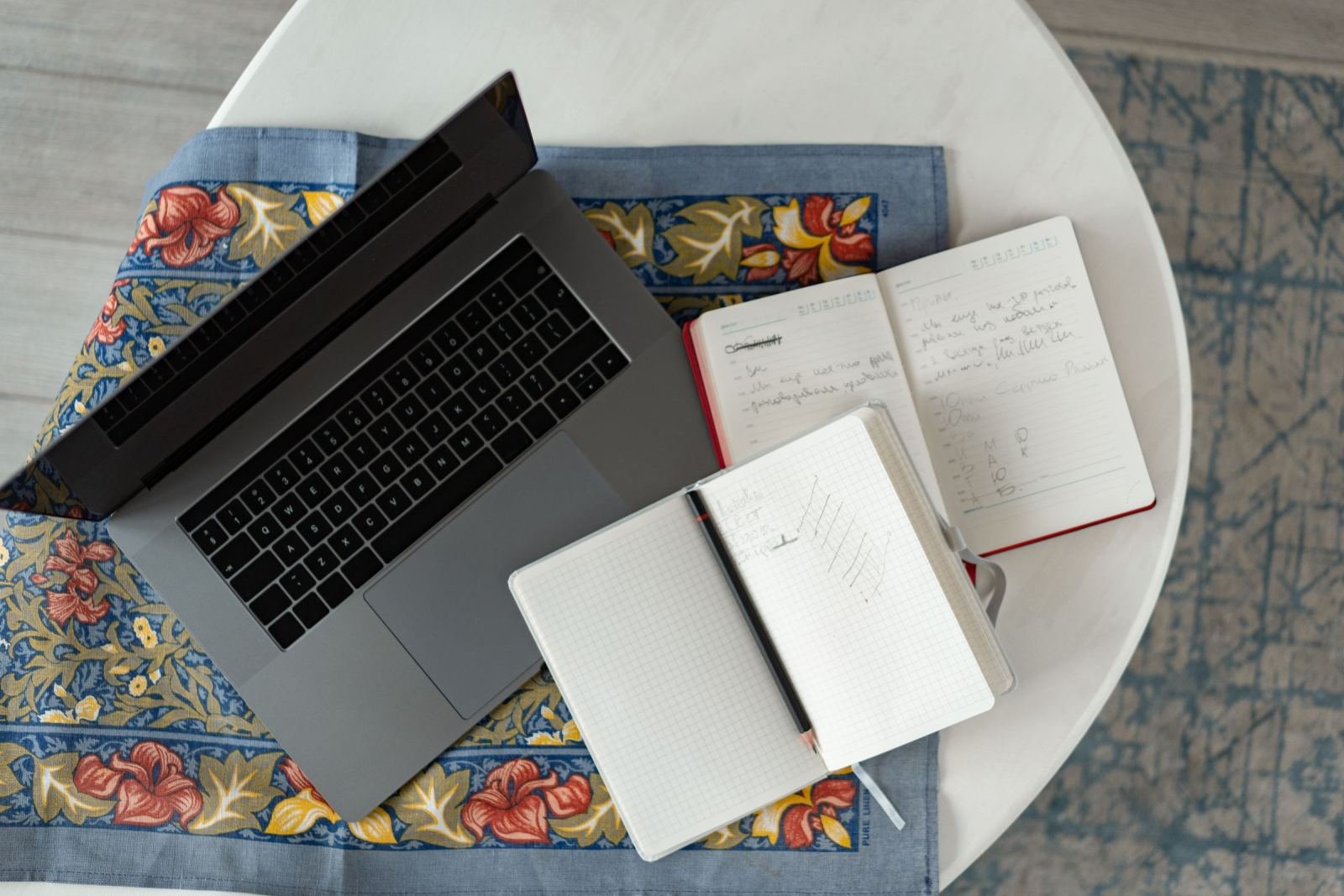 A laptop and two open notebooks with handwritten notes on a white table