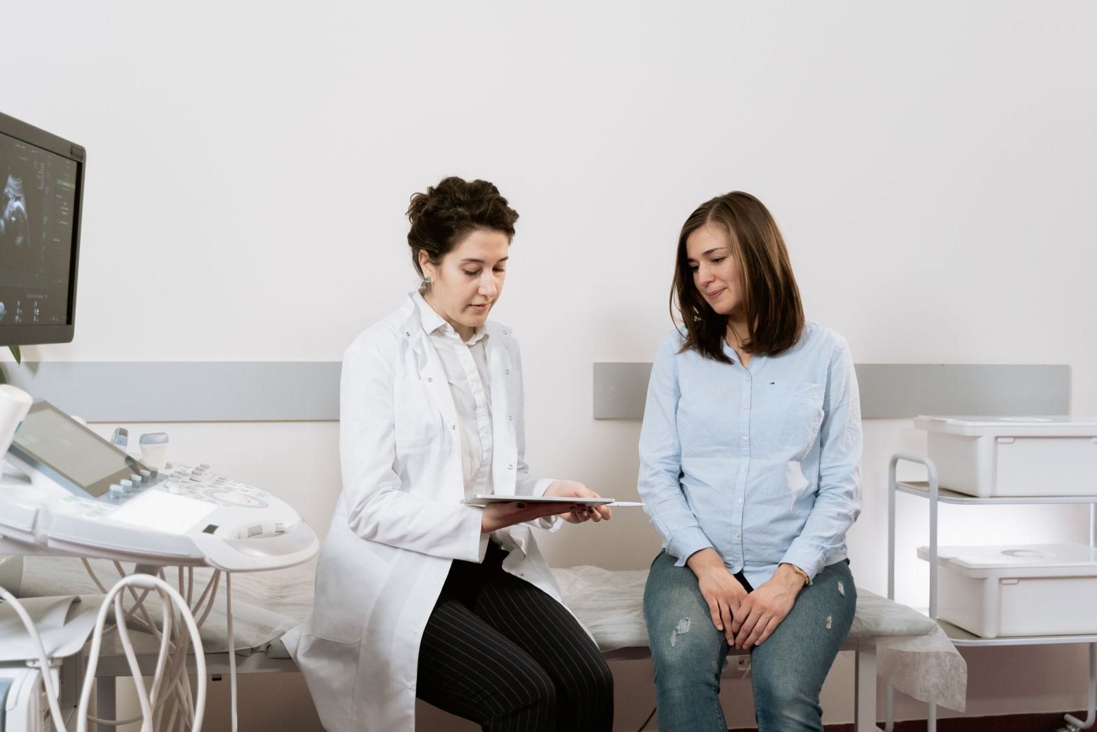 A clinician in a white coat shows a screen to a pregnant patient.