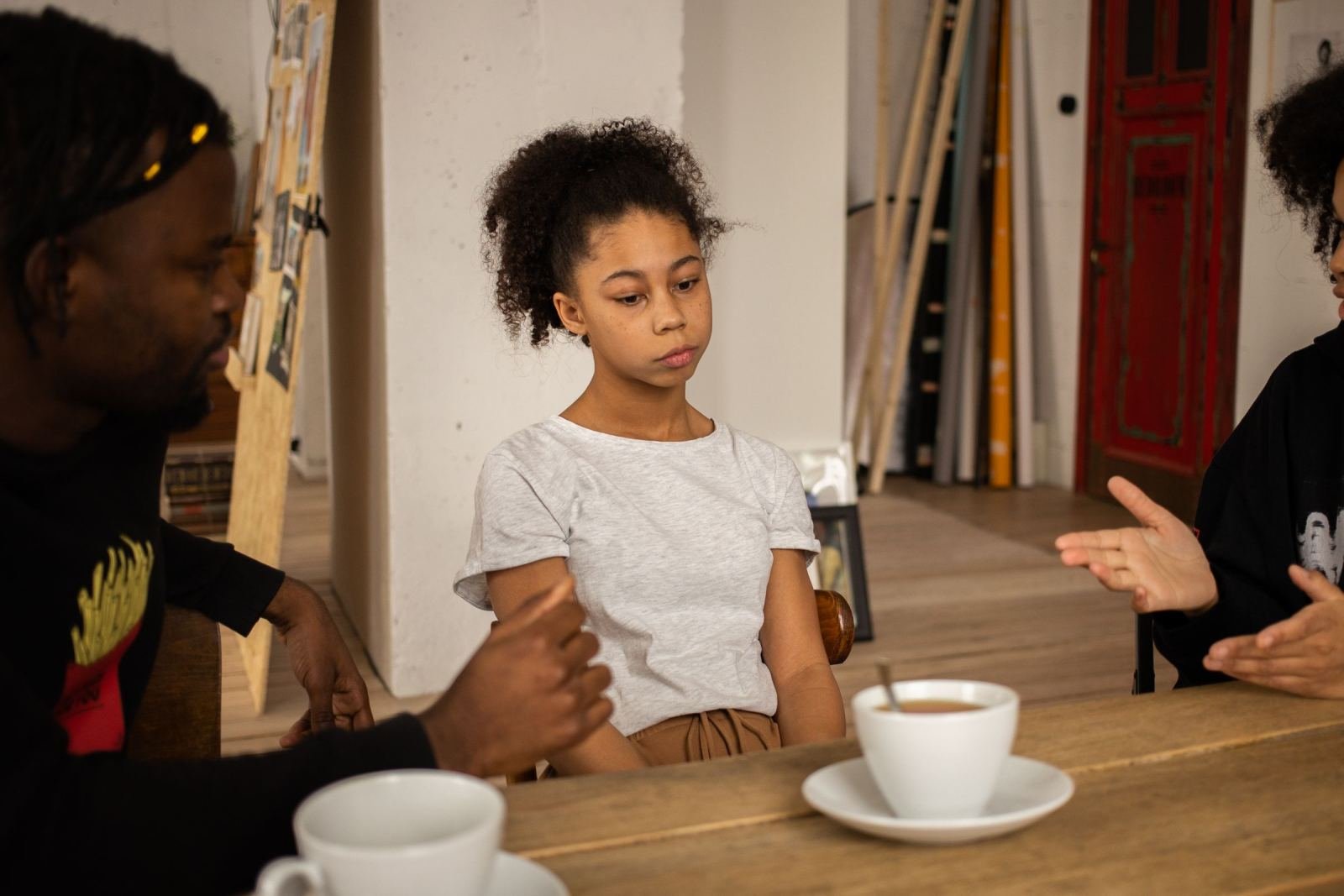 Two adults sit across from a teen girl at a wood table.