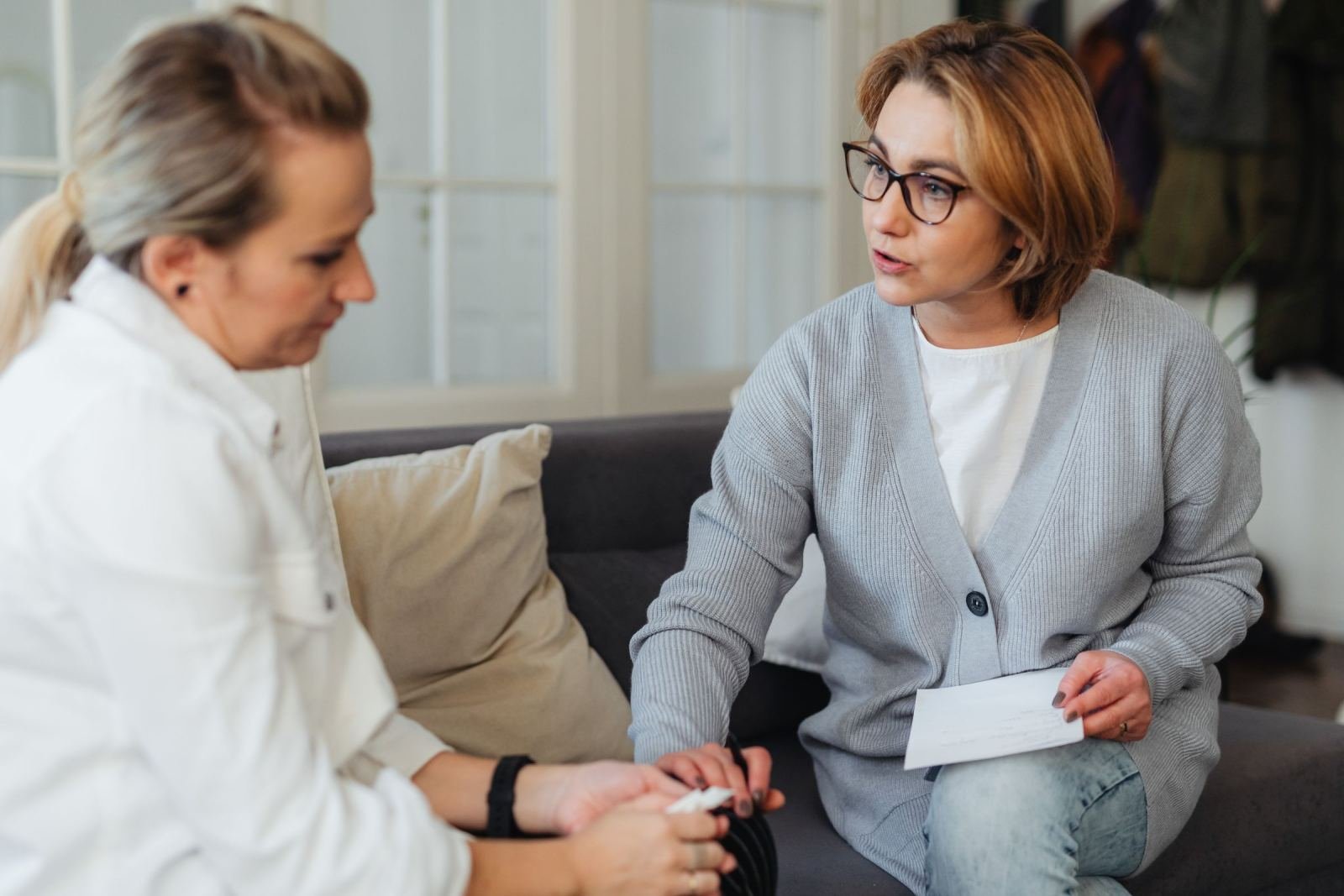 Two women sit on a sofa discussing a piece of paper