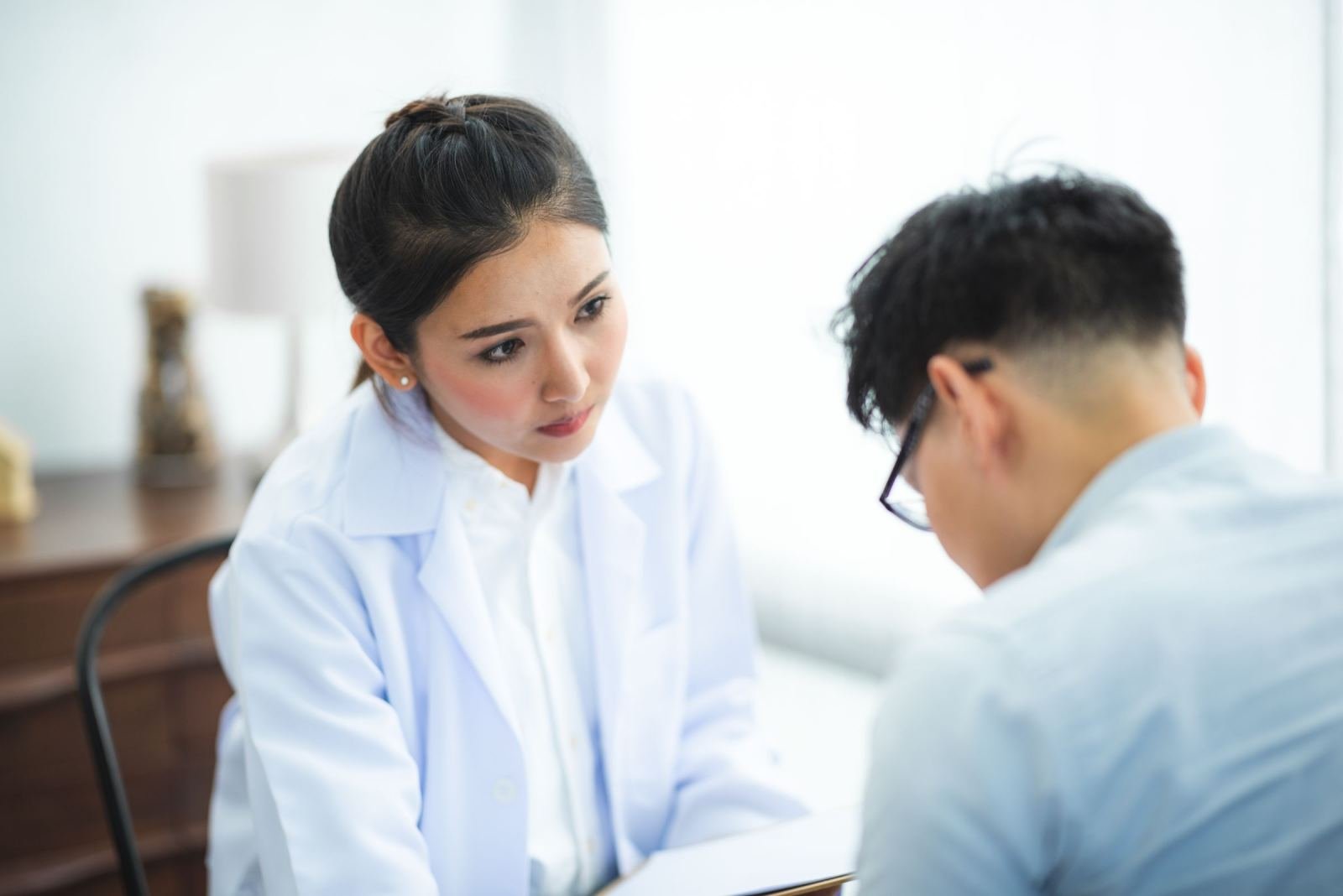 A doctor in a white coat talks to a patient at a clinic.