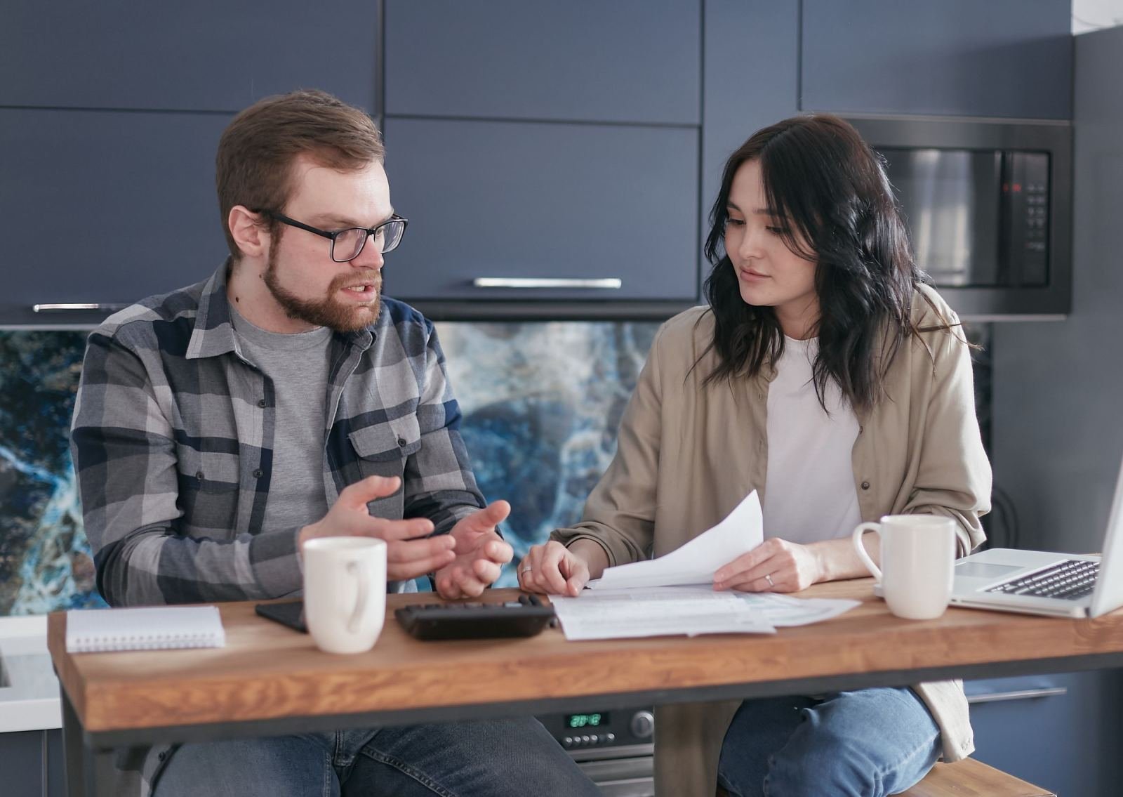A man and woman review documents and a calculator at a kitchen table