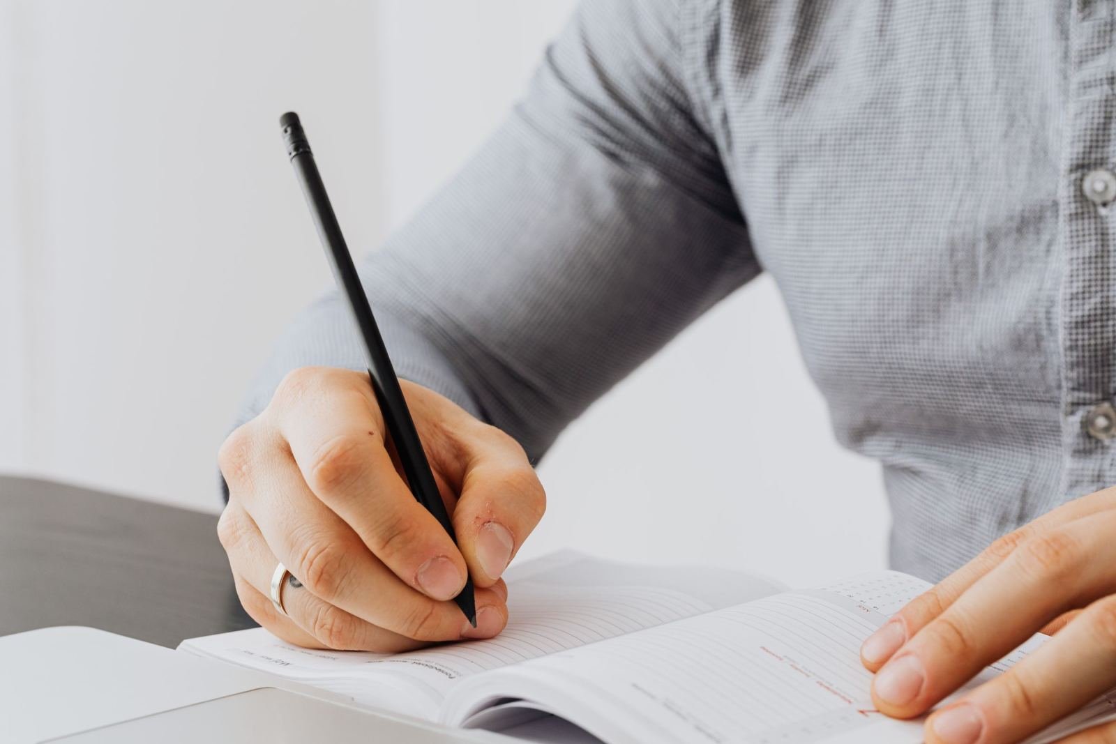 A person in a grey shirt writes in a notebook with a black pen