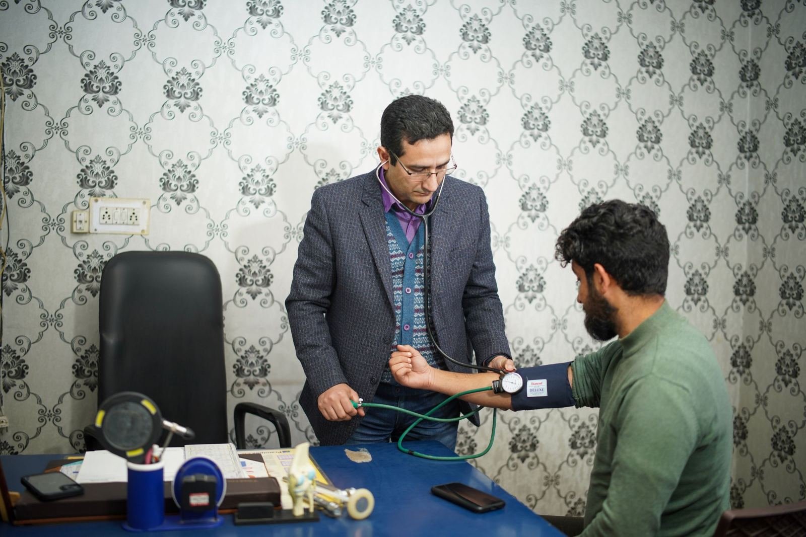 A doctor uses a blood pressure cuff on a patient's arm in an exam room