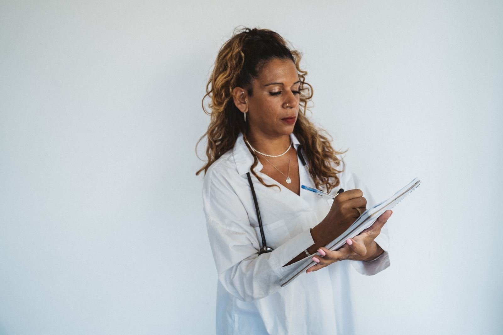 A healthcare professional in a white coat and stethoscope writing in a notebook