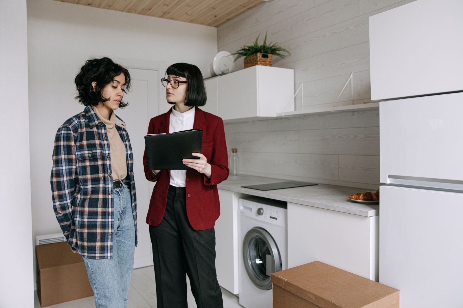 Two women in a white kitchen, one holding a tablet and talking to the other