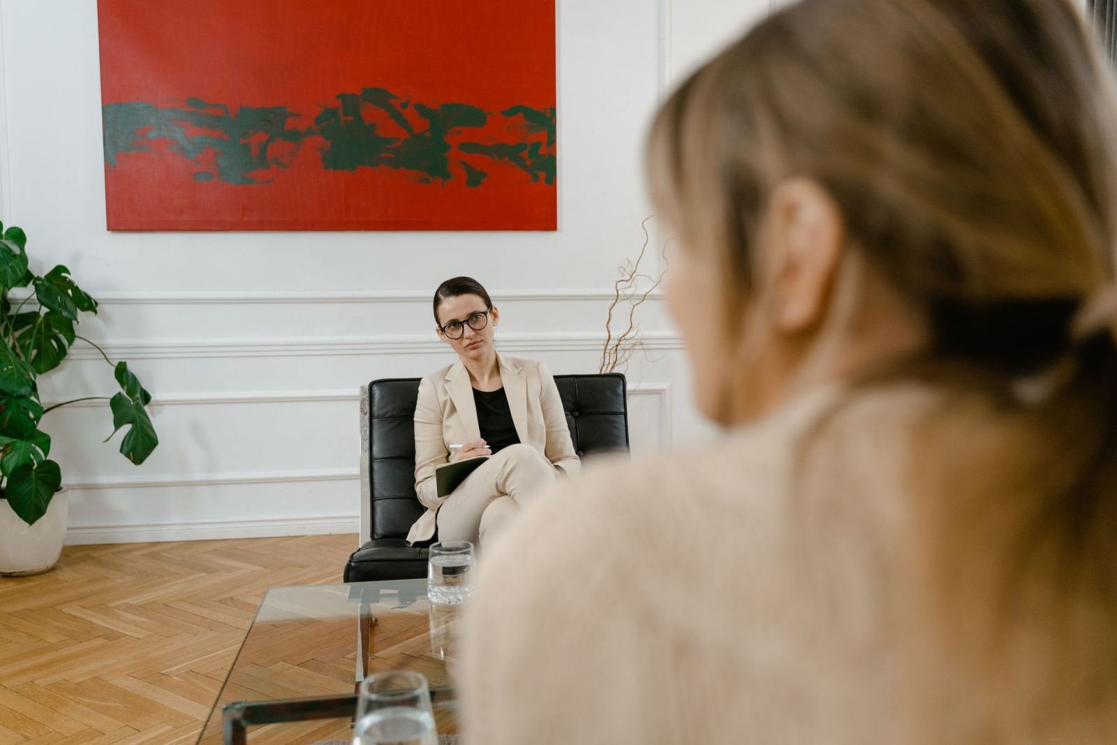 A counselor in a beige blazer sits on a black sofa and listens to a client