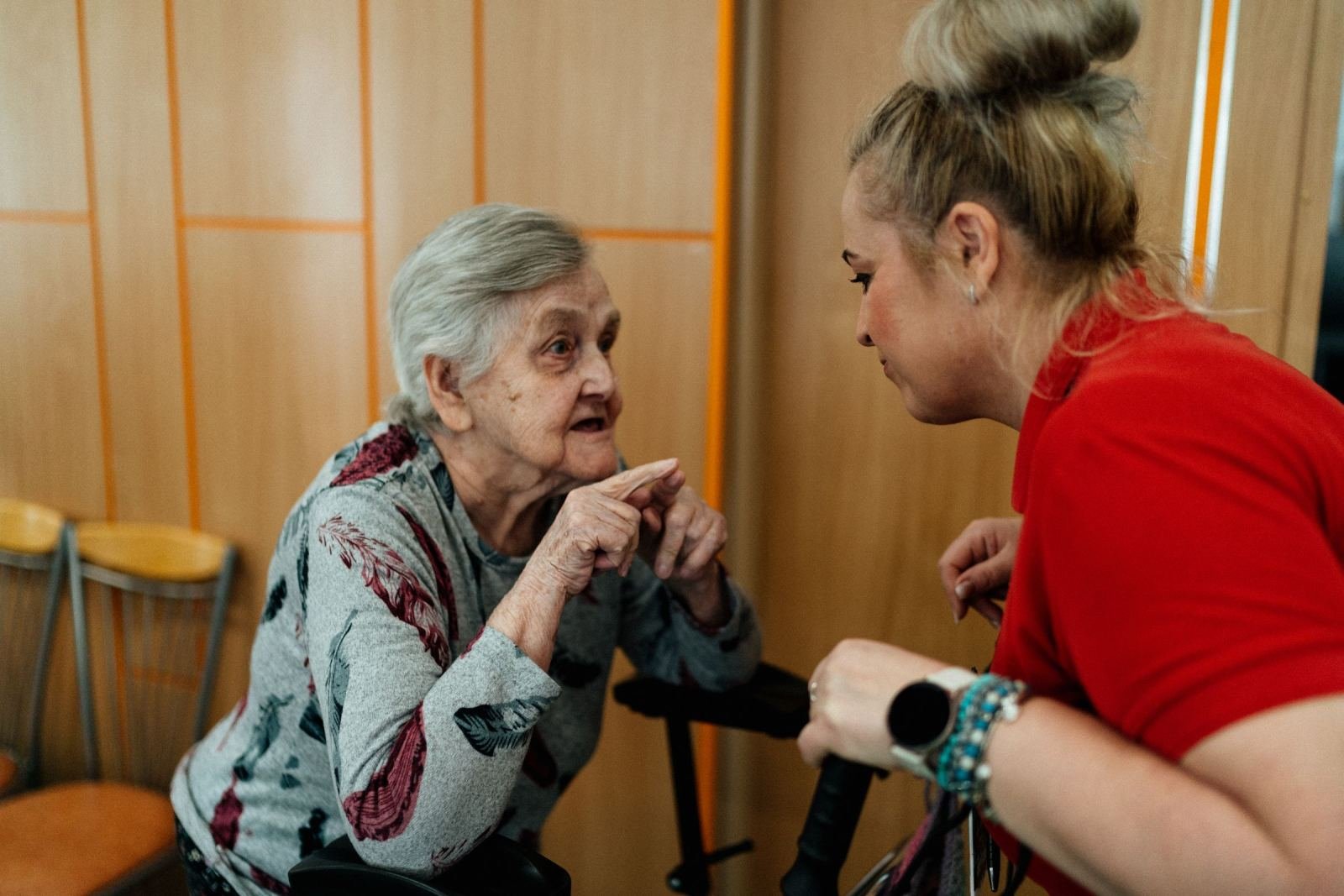 An older woman gestures while talking to a younger woman in a red shirt