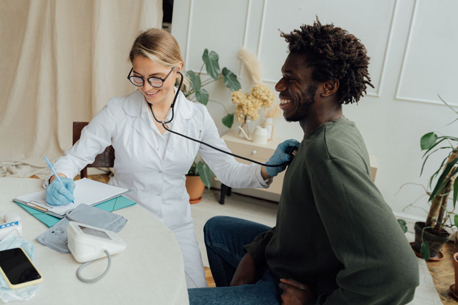 A man smiles while a doctor in a white coat uses a stethoscope to check him.